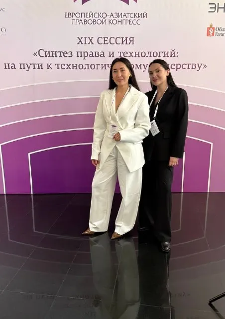 ЕАПК 2026: Ксения (справа, чёрный костюм) с коллегой в белом костюме у пресс-волла XIX сессии